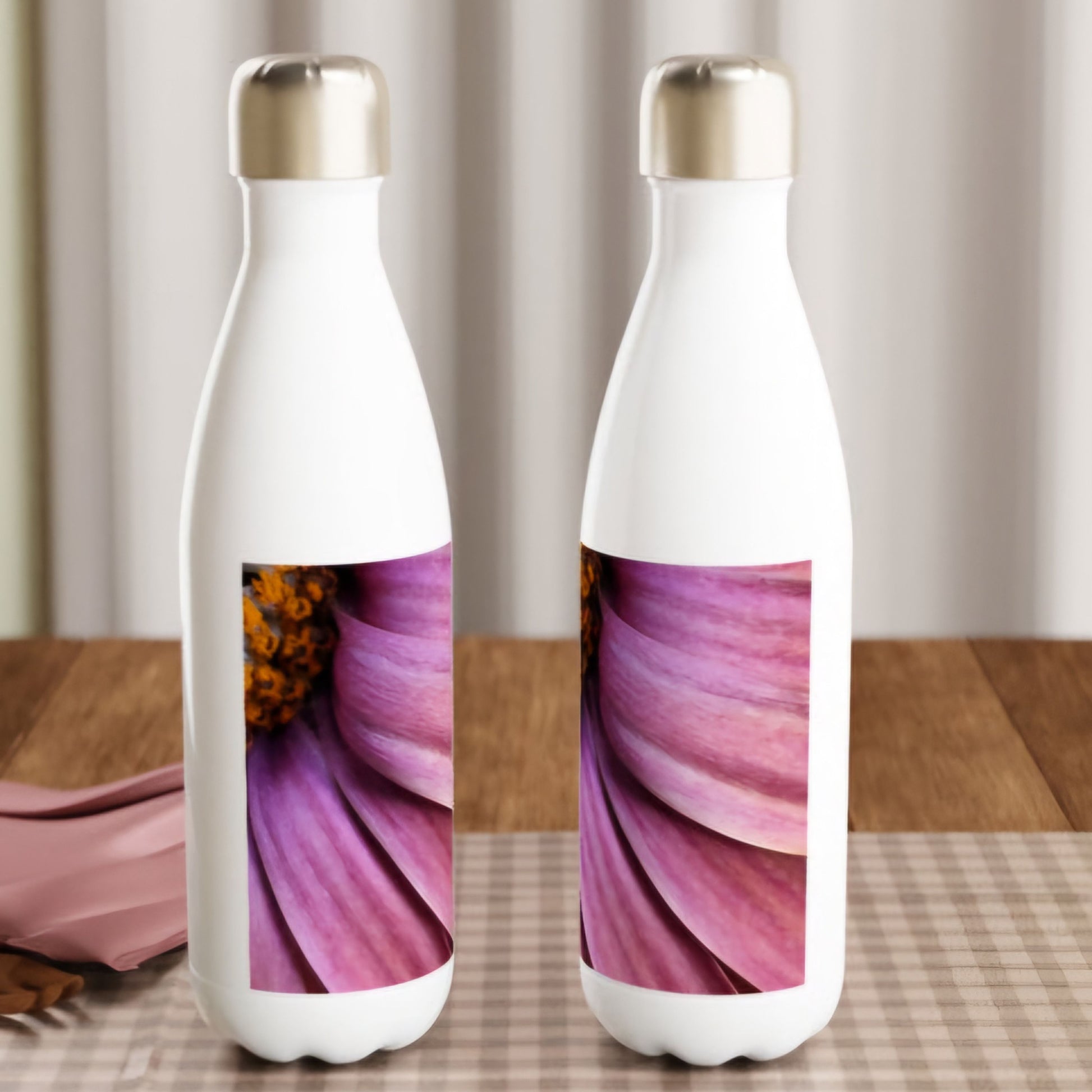 Two white water bottles on wooden surface. Bottles has silver corc on and they have a printed picture on. Closeup Photograph of a star-eyed-flower in lush pink and vivid orange center.